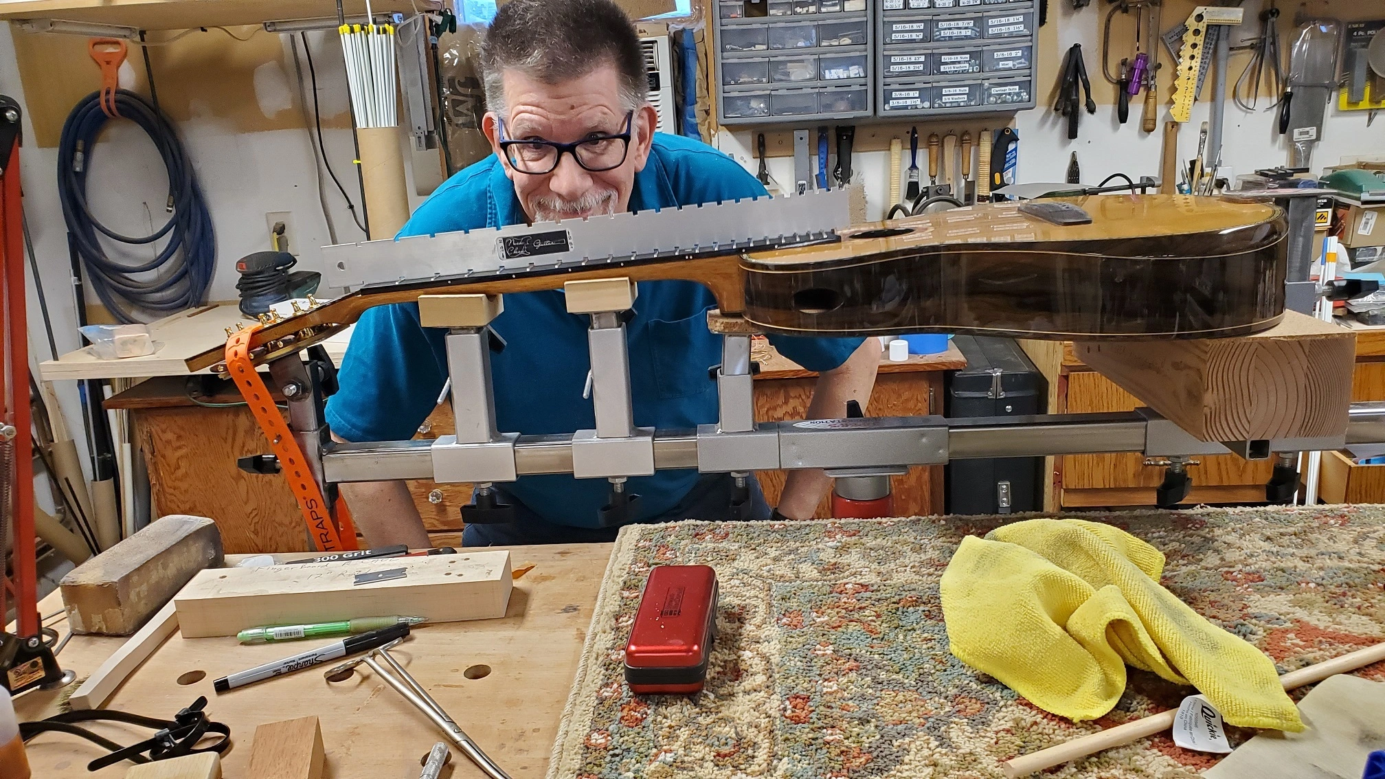Luthier smiling behind a guitar neck being fitted during construction in a workshop