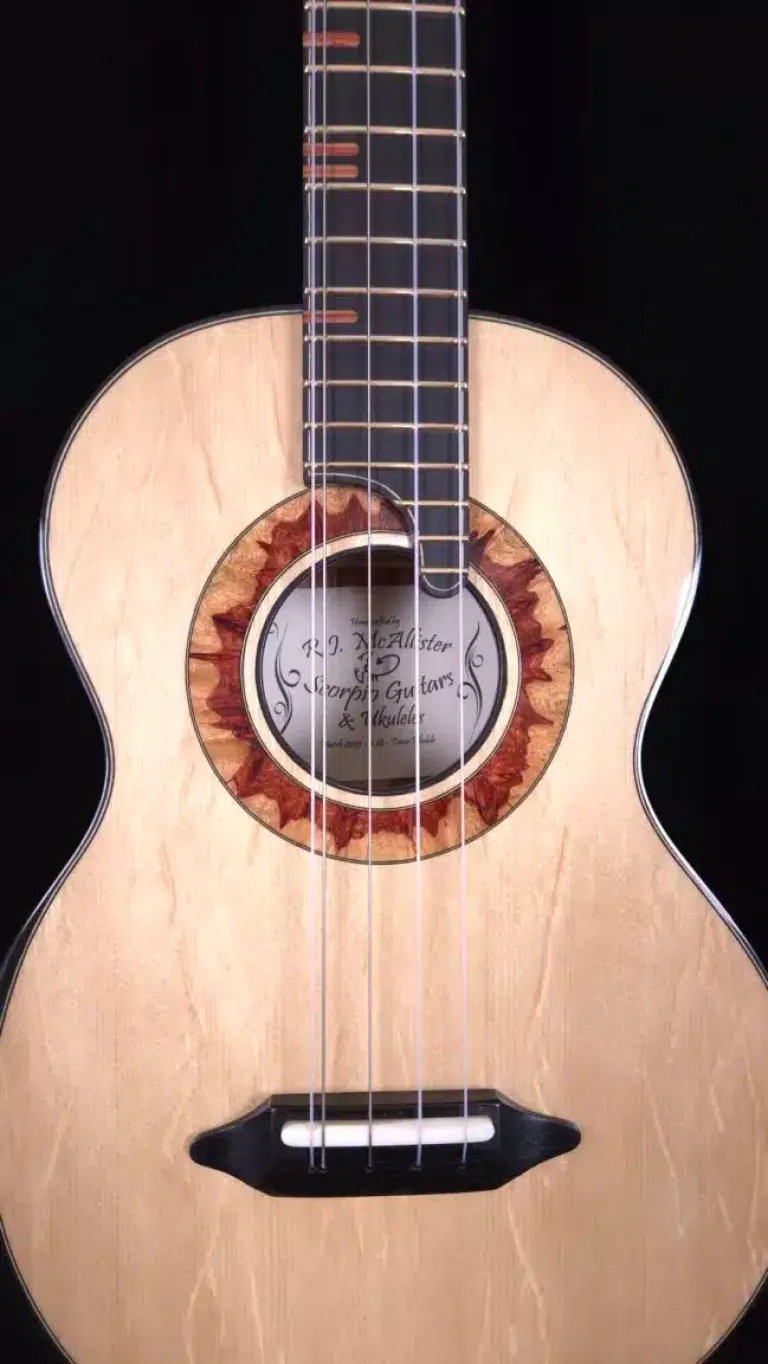 Close-up of a custom ukulele top showing the soundhole rosette, strings, fretboard, and bridge.