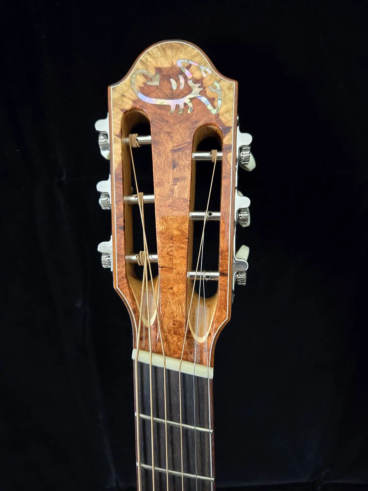 Front view of a classical guitar headstock with slotted design, wood grain, and tuning machines.