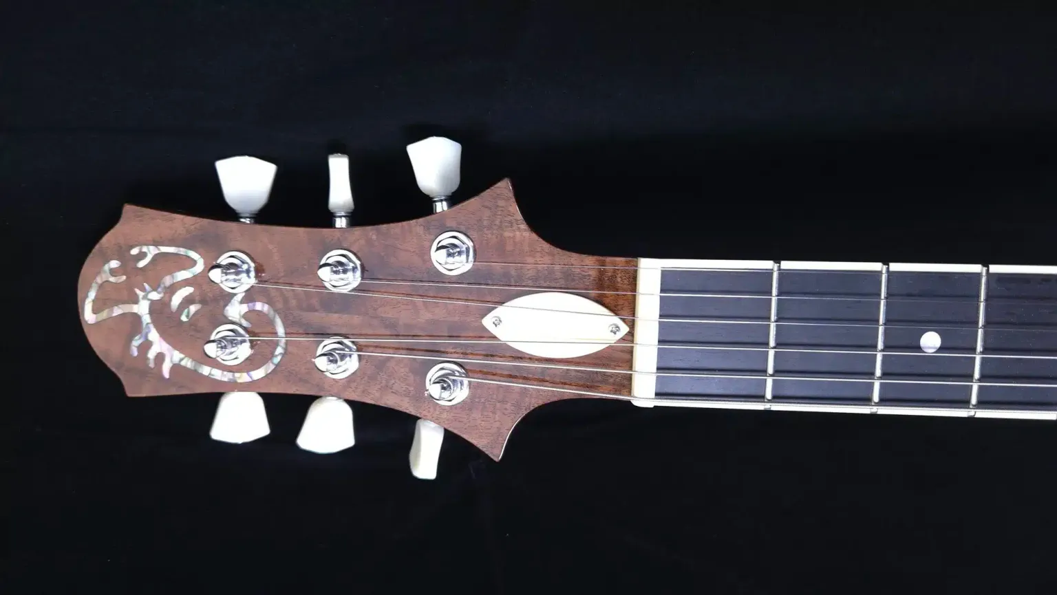 Close-up of a custom guitar headstock featuring decorative inlay, chrome tuning machines, and a dark fingerboard.