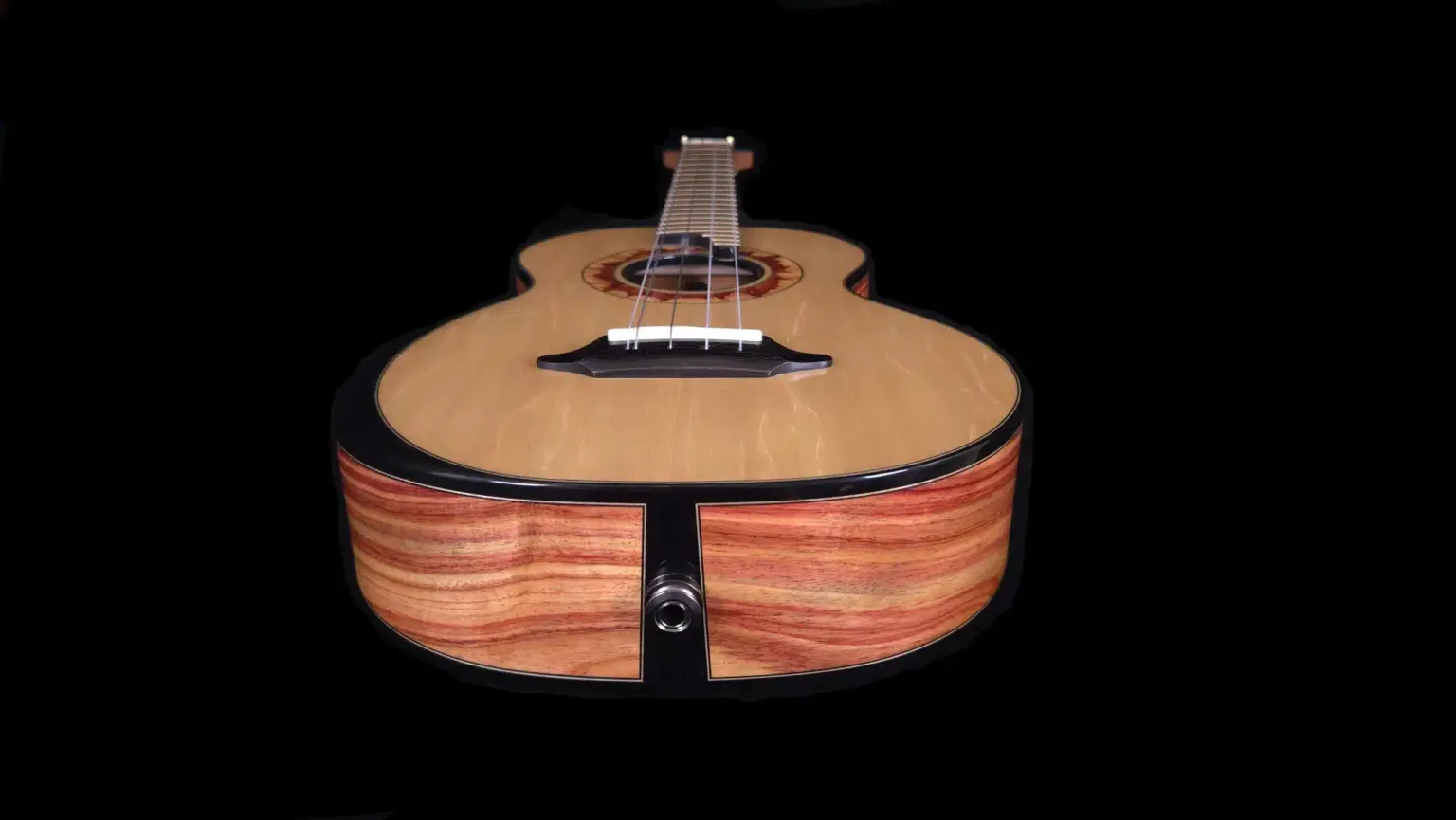 Front view of a custom ukulele showing the end block, side wood grain, and glossy finish against a black background.