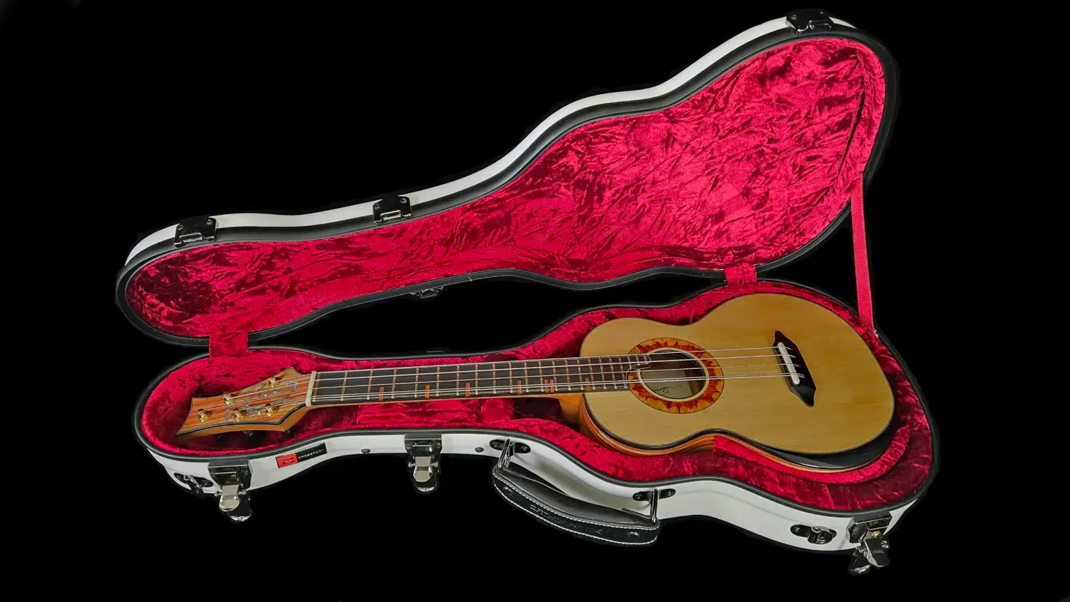 Custom ukulele resting inside an open hardshell case with red plush interior and fitted contours.