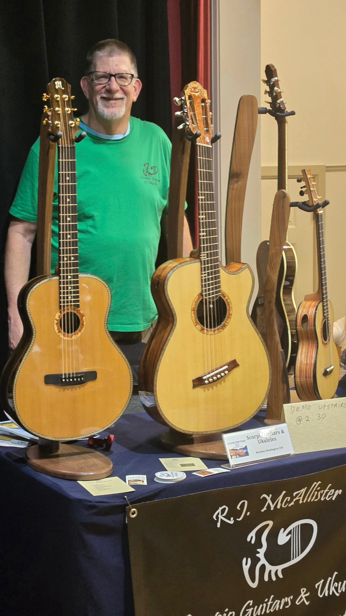 Luthier standing behind a display of handcrafted acoustic guitars at a guitar show