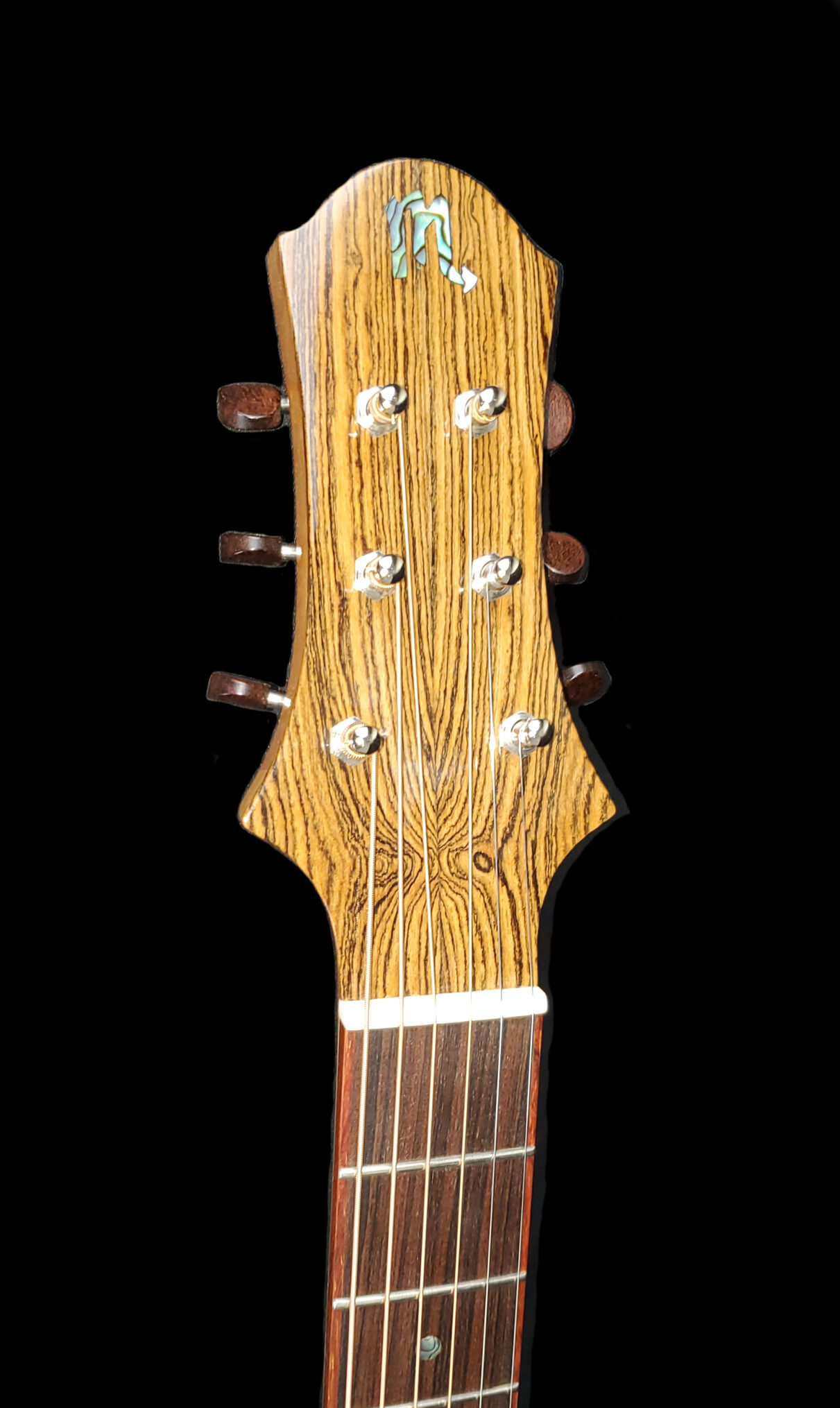 Front view of an acoustic guitar headstock with striped wood grain, tuning pegs, and inlaid logo.