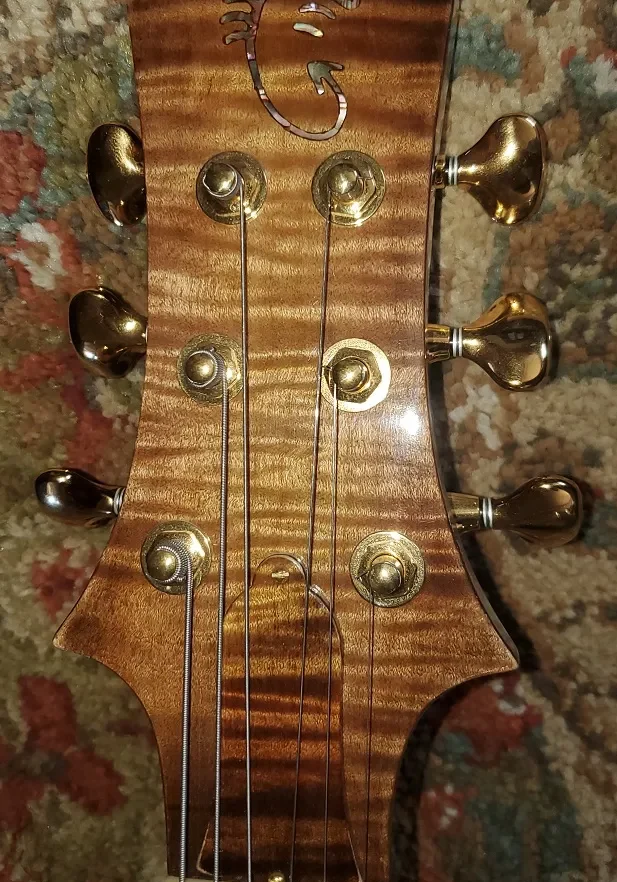 Close-up of an acoustic guitar headstock made from flamed wood with gold tuning machines.