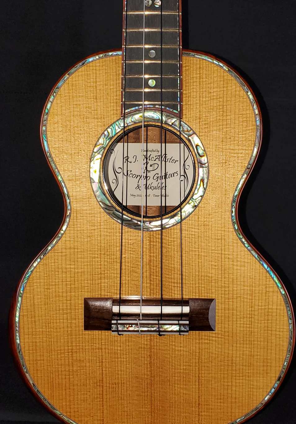 Concert ukulele with light wood top, abalone rosette, dark fingerboard, and wood bridge.
