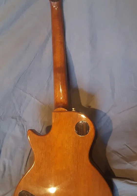 Back view of an acoustic guitar showing a glossy wood finish, neck, and gold tuning machines.