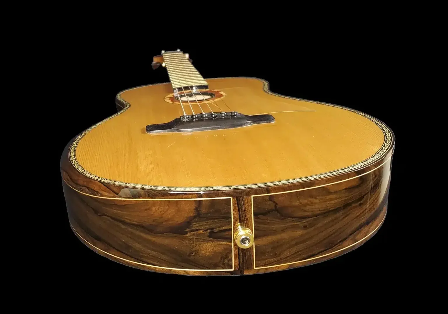 Low-angle view of a custom acoustic guitar showing the end block, tail jack, and figured wood sides.