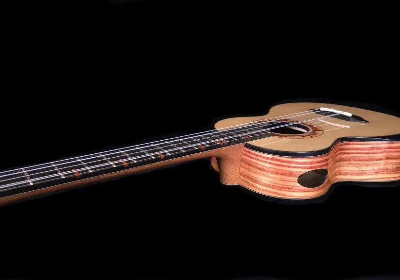 Angled side view of a handcrafted ukulele with layered wood sides and side sound port